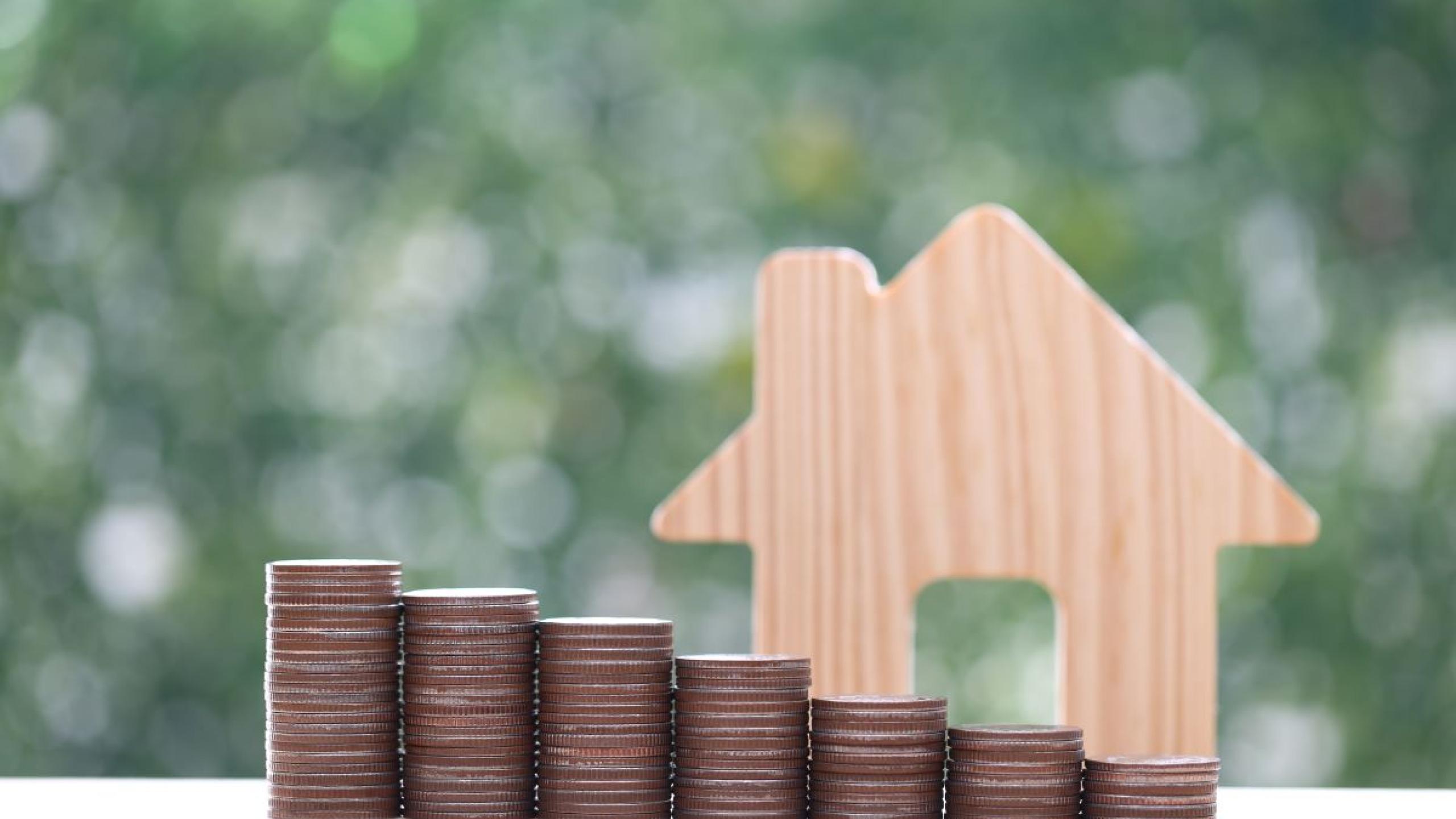 Houten schaalmodel van huis met stapel munten.