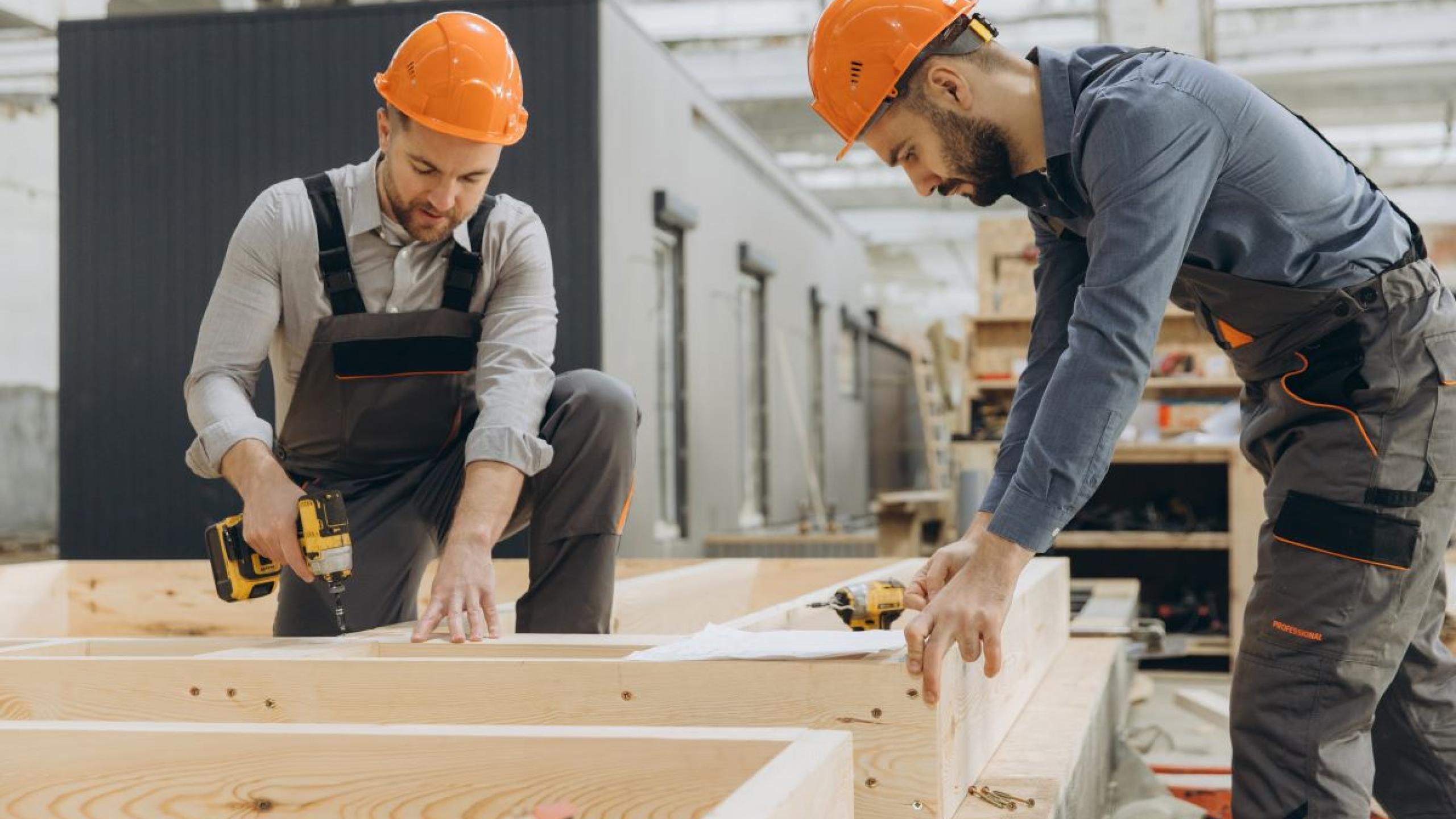 Twee mannen werken in aterlier aan houten structuur van modulair huis.