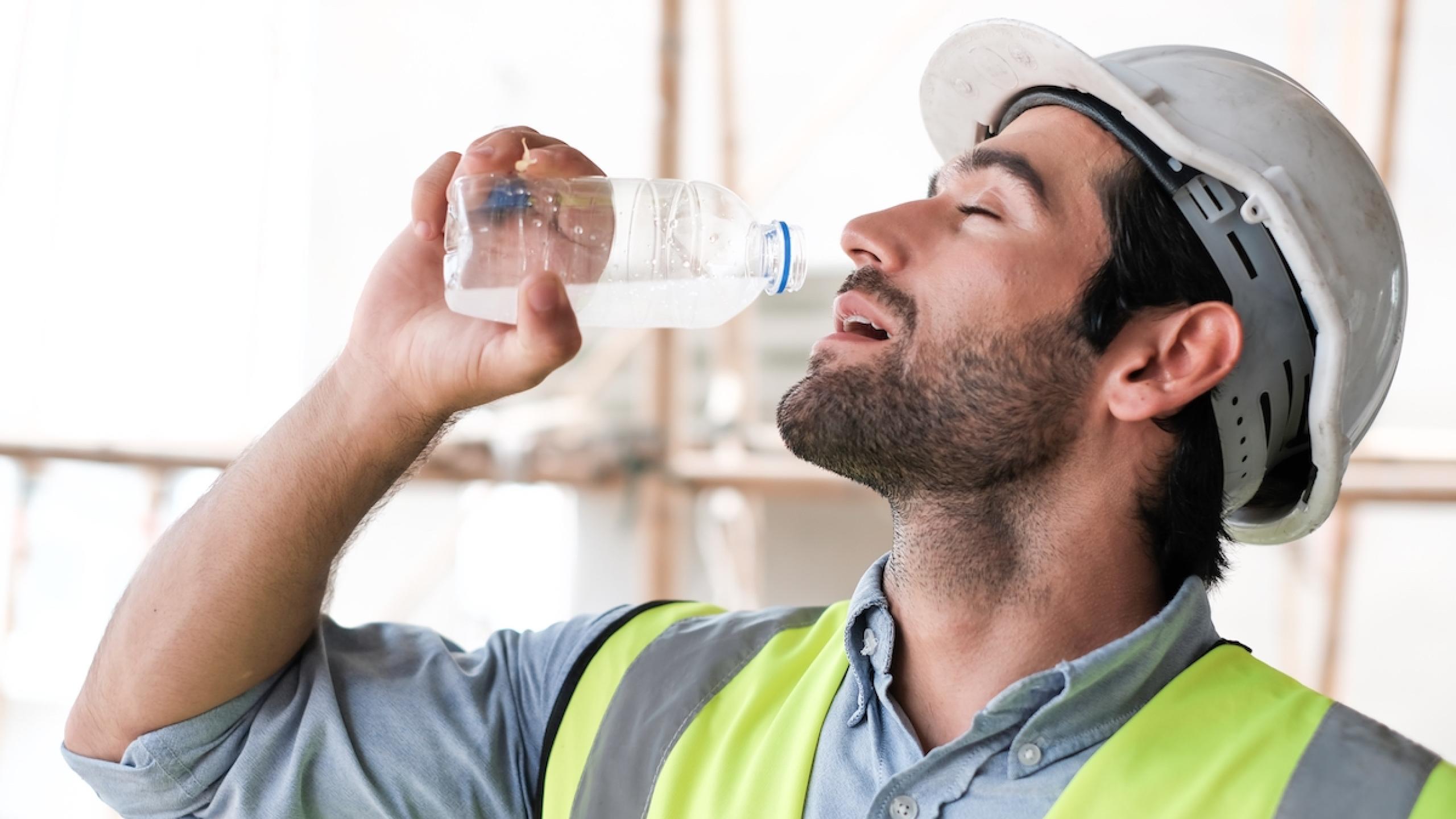 Man met fluohesje drink een fles water.