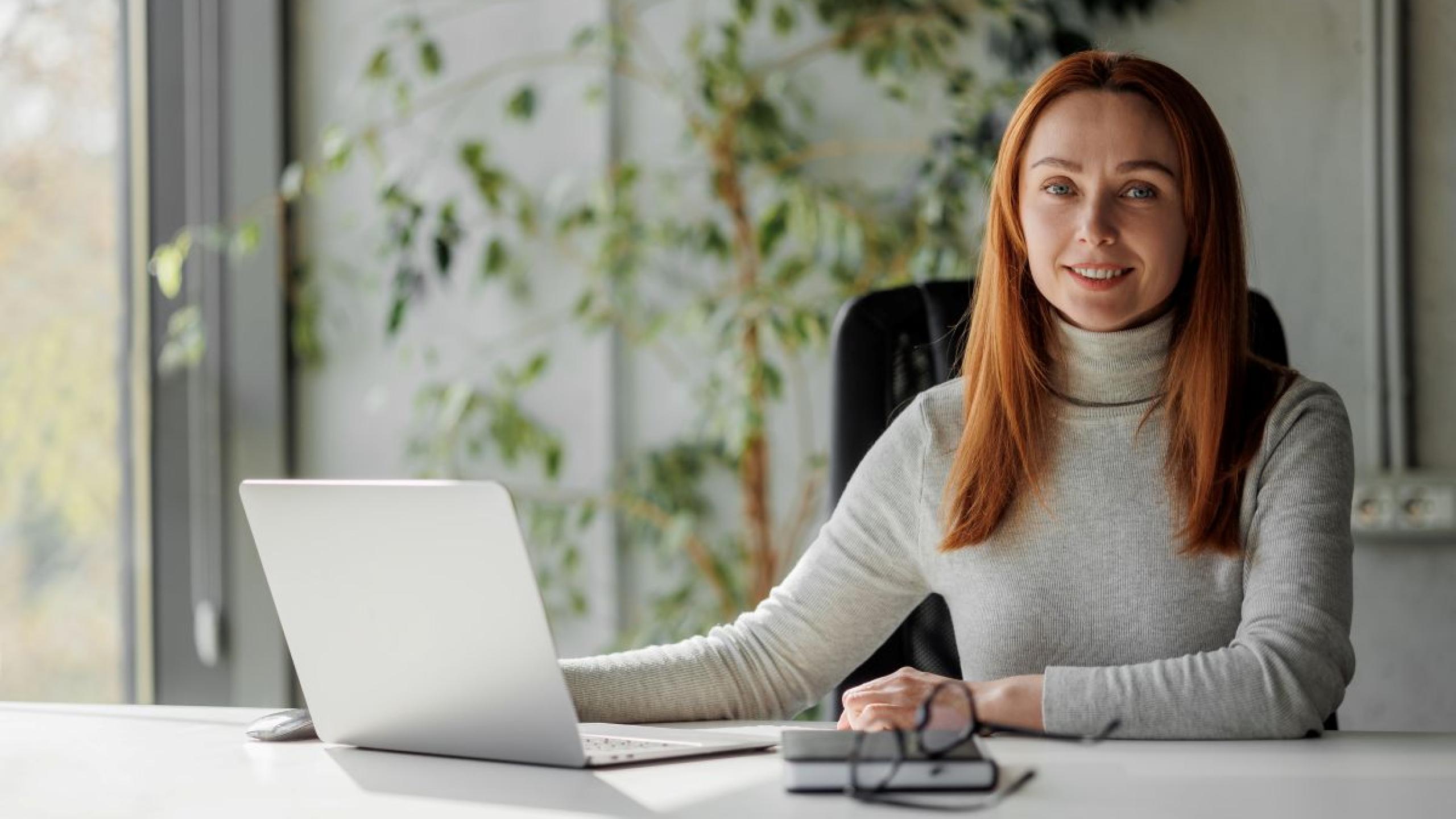 Jonge vrouw met laptop aan bureau.