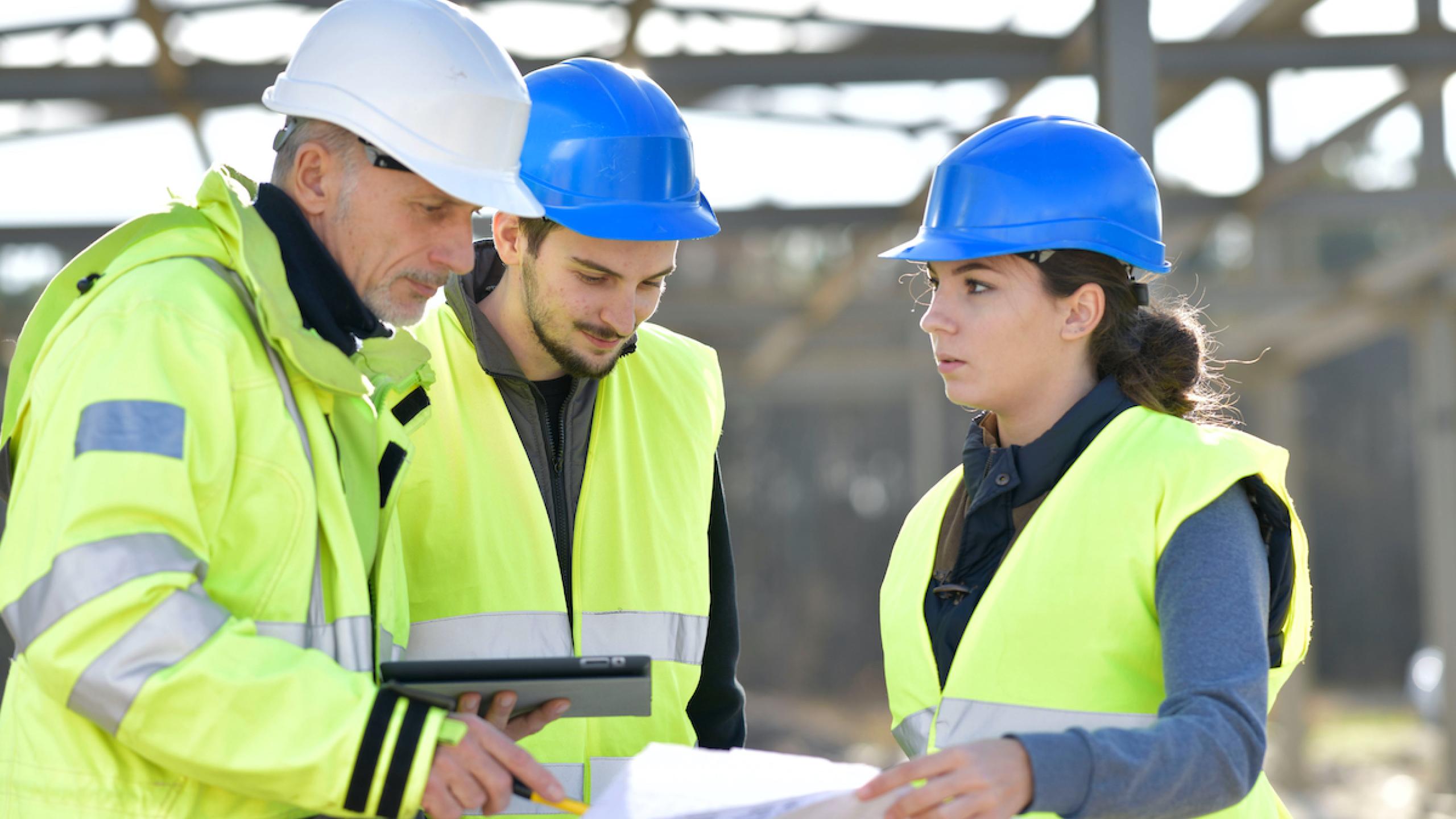 Twee studenten met begeleider op bouwplaats.