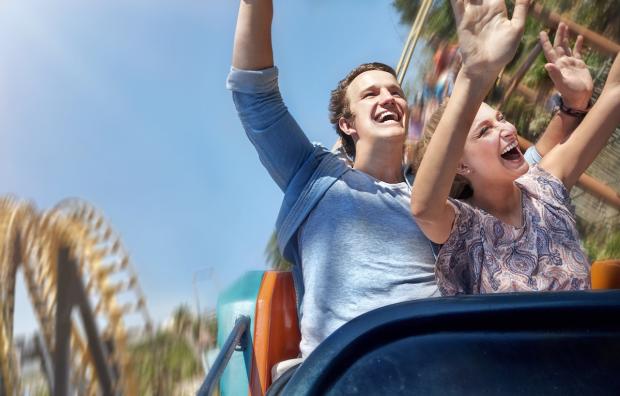 Man en vrouw met de handen omhoog in een rollercoaster.